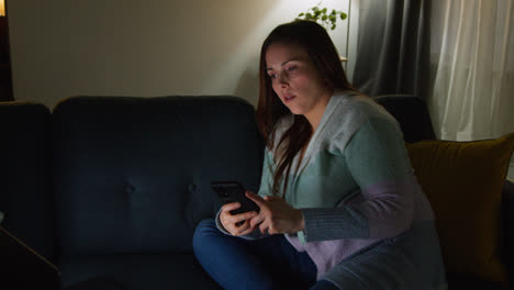 Mujer-Sentada-En-Un-Sofá-En-Casa-Por-La-Noche-Transmitiendo-O-Viendo-Películas-O-Programas-En-Una-Computadora-Portátil-Y-Navegando-Por-Internet-En-El-Teléfono-11